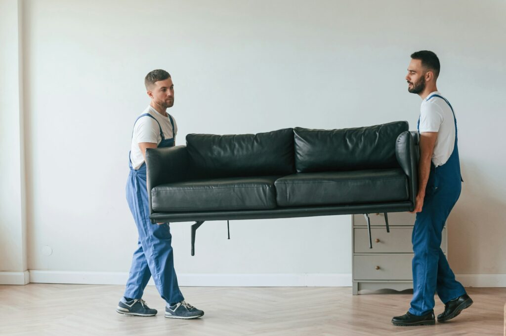 Sofa in hands. Two moving service employees in a room