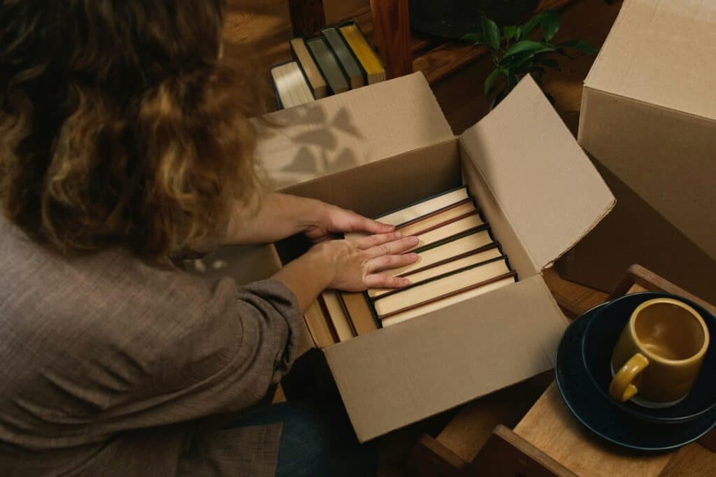 Relocation, movement. Young woman packing books in moving box.