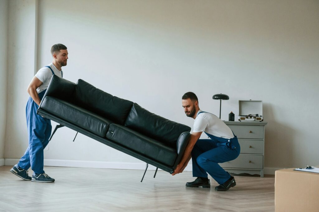 Sofa in hands. Two moving service employees in a room