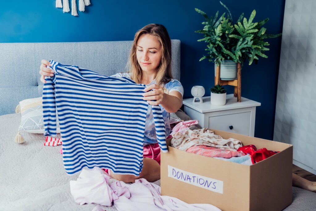 Woman selecting clothes from her wardrobe for donating to a Charity shop. Decluttering